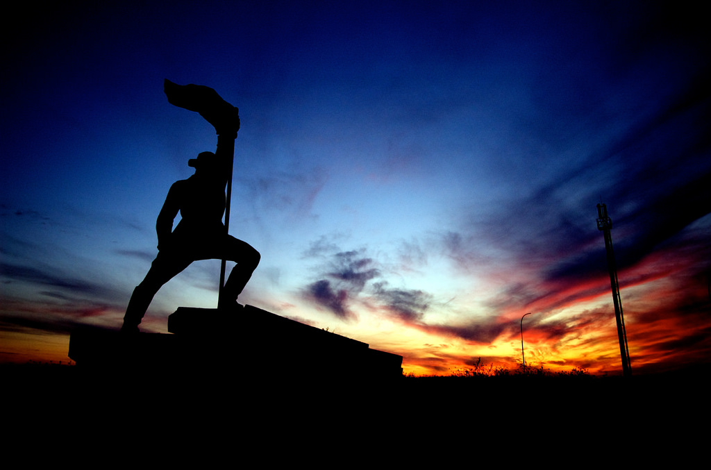 A monument of a man heroically brandishing a flag built in memory of the liberators of Ukraine during World War 2 on the border between Užhorod and Vyšné Nemecké.  It is sunset.